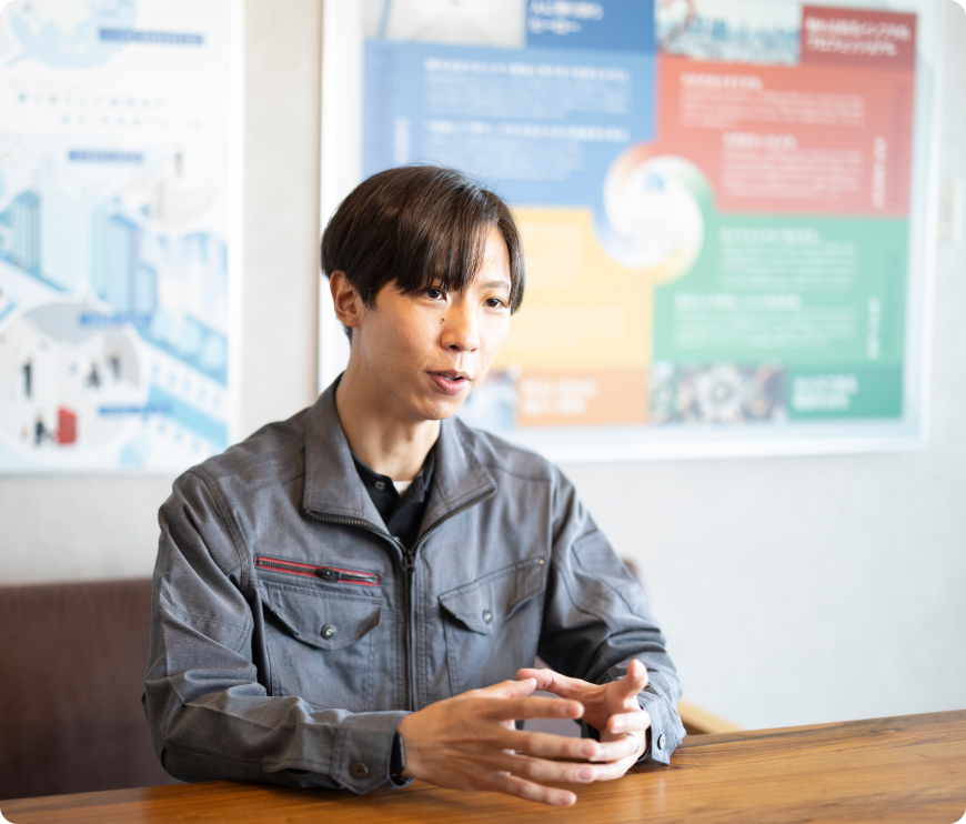 作業着を着用した、インタビューを受ける鈴木一郎氏の写真