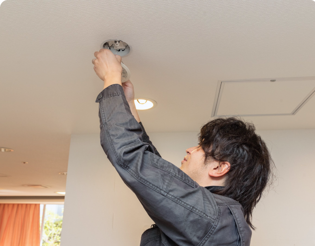 天井の照明器具(ダウンライト)の設置・点検を丁寧に行う技術スタッフ。建物の安全と快適を支えるプロの現場。