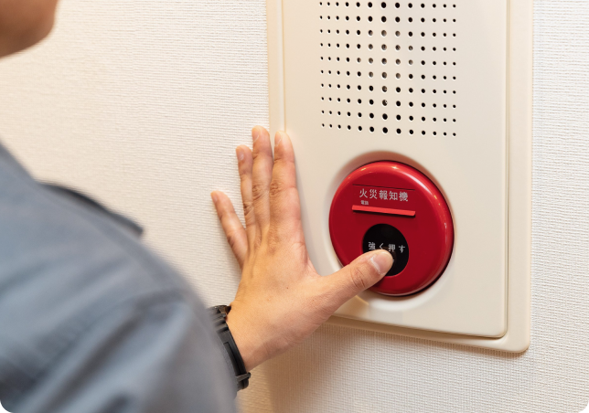 火災報知機の動作確認を行う技術者の手元。一瞬の油断も許さない、厳格な設備メンテナンスのイメージ。