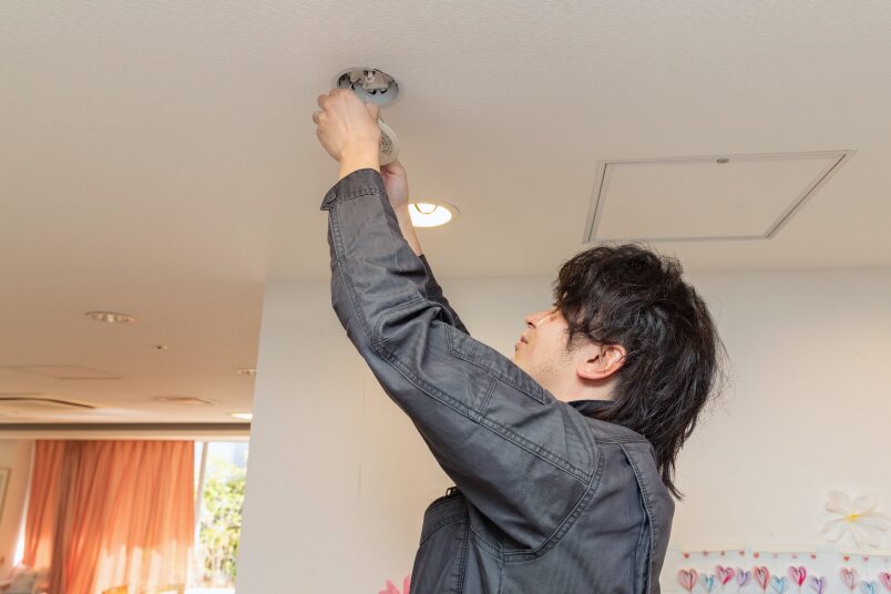 天井の照明器具(ダウンライト)の設置・点検を丁寧に行う技術スタッフ。建物の安全と快適を支えるプロの現場。