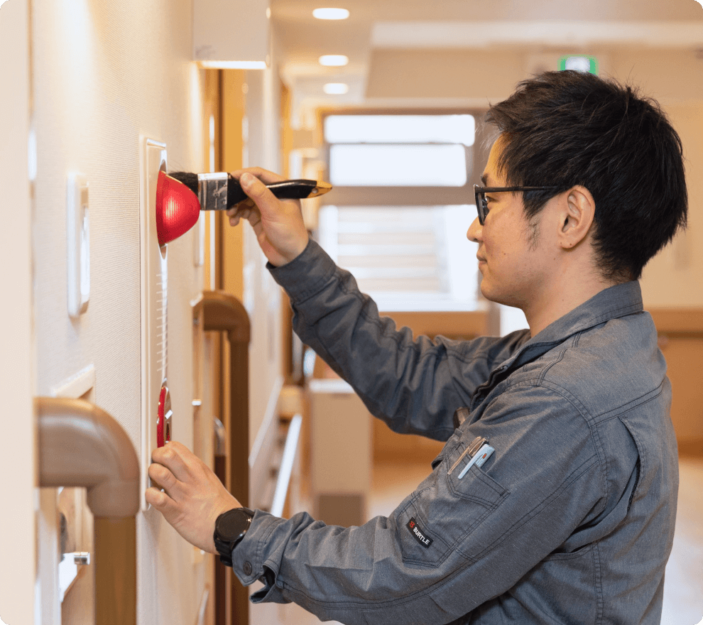 施設内の火災報知器を専用のブラシで丁寧に清掃・点検する技術スタッフ。細部まで妥協しない保守管理が、建物の安全と安心を支える。