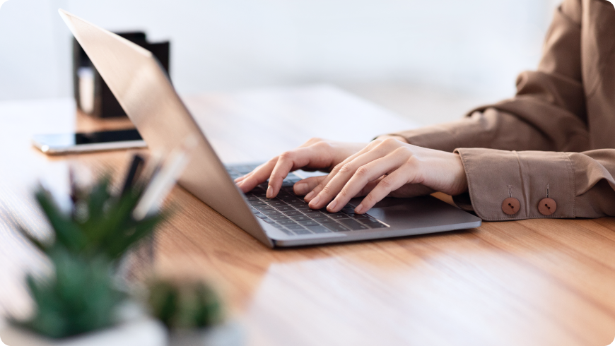 木目調のデスクで集中してPC作業を行う手元のアップ。場所を選ばない柔軟な働き方と、生産性の高い業務環境。