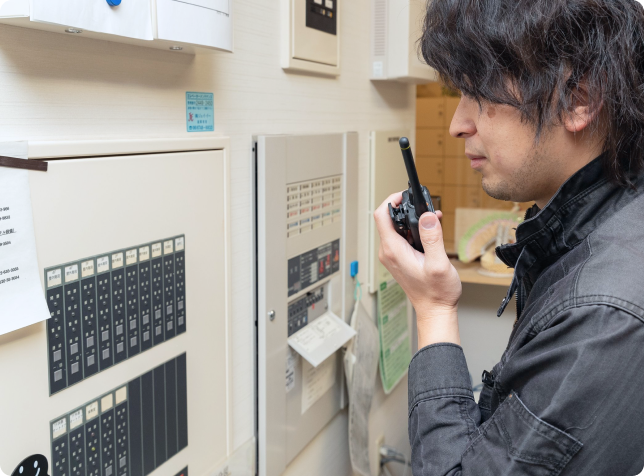 制御盤の前で無線機(トランシーバー)を使い、迅速に連絡を取り合う現場スタッフ。連携の取れたチームワークの象徴。