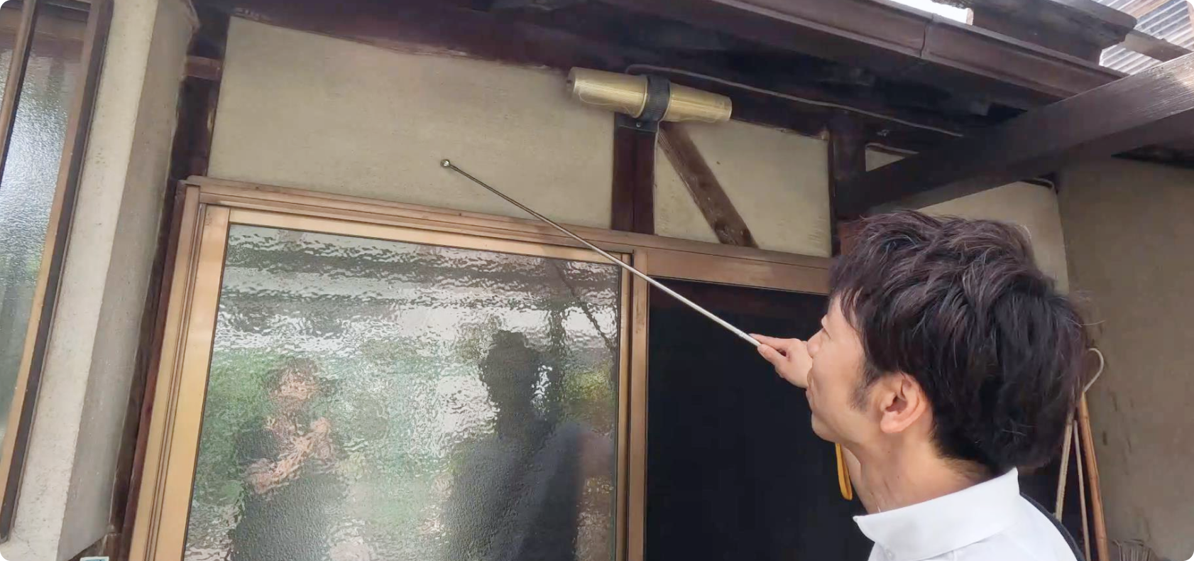 伸縮式の打診棒で伝統的な建物の外壁を検査するプロの技術者。経験に裏打ちされた感触で、構造の健全性を細かくチェック。