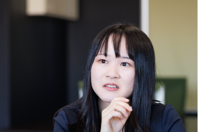 仕事への想いややりがいを真剣な表情で語る、スーツ姿の女性社員。社員インタビューのワンシーン。