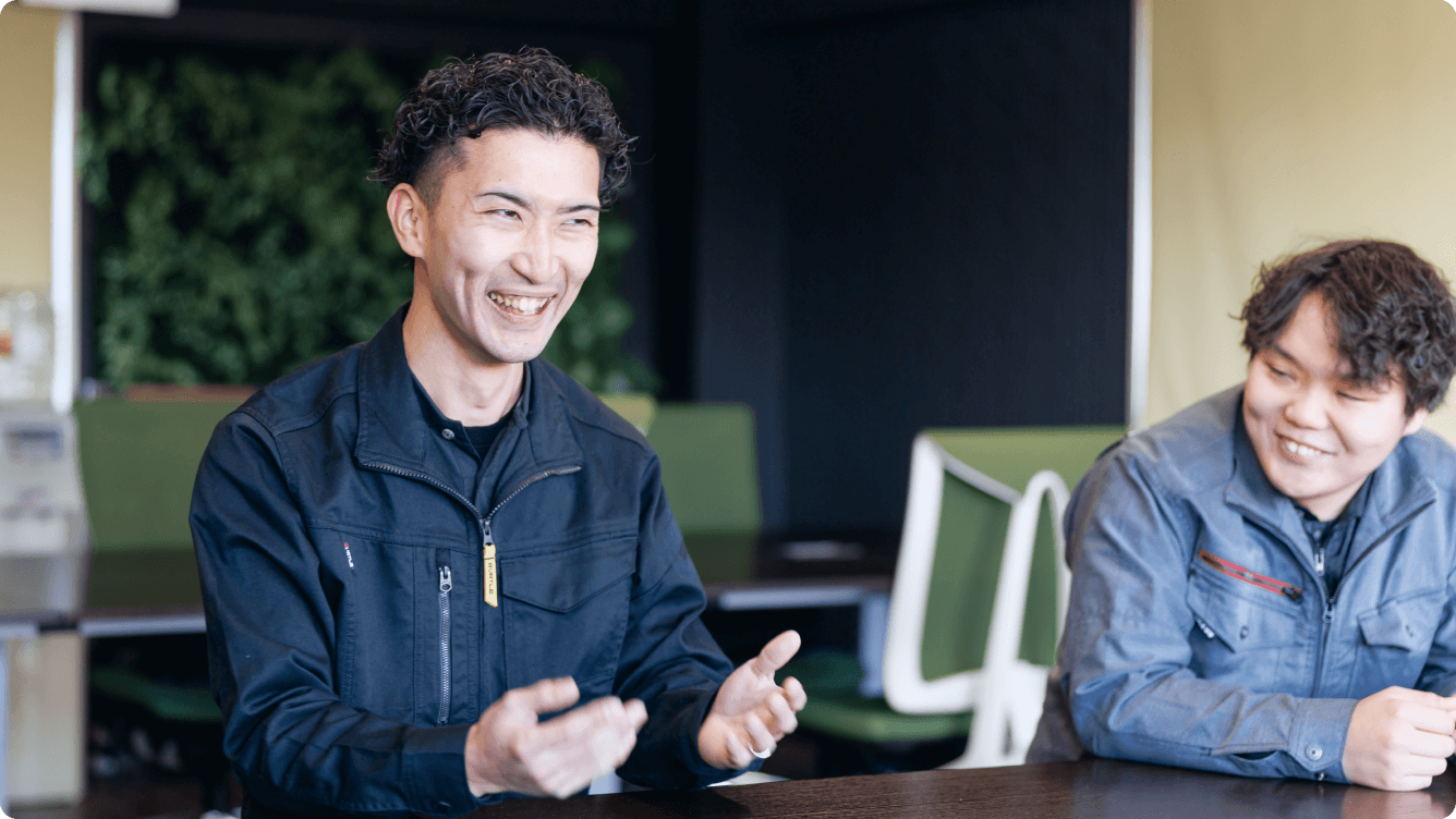 作業着姿で笑顔で語り合う2名のスタッフ。ベテランから若手まで、気軽に相談し合える「家族のようなあたたかい関係性」。