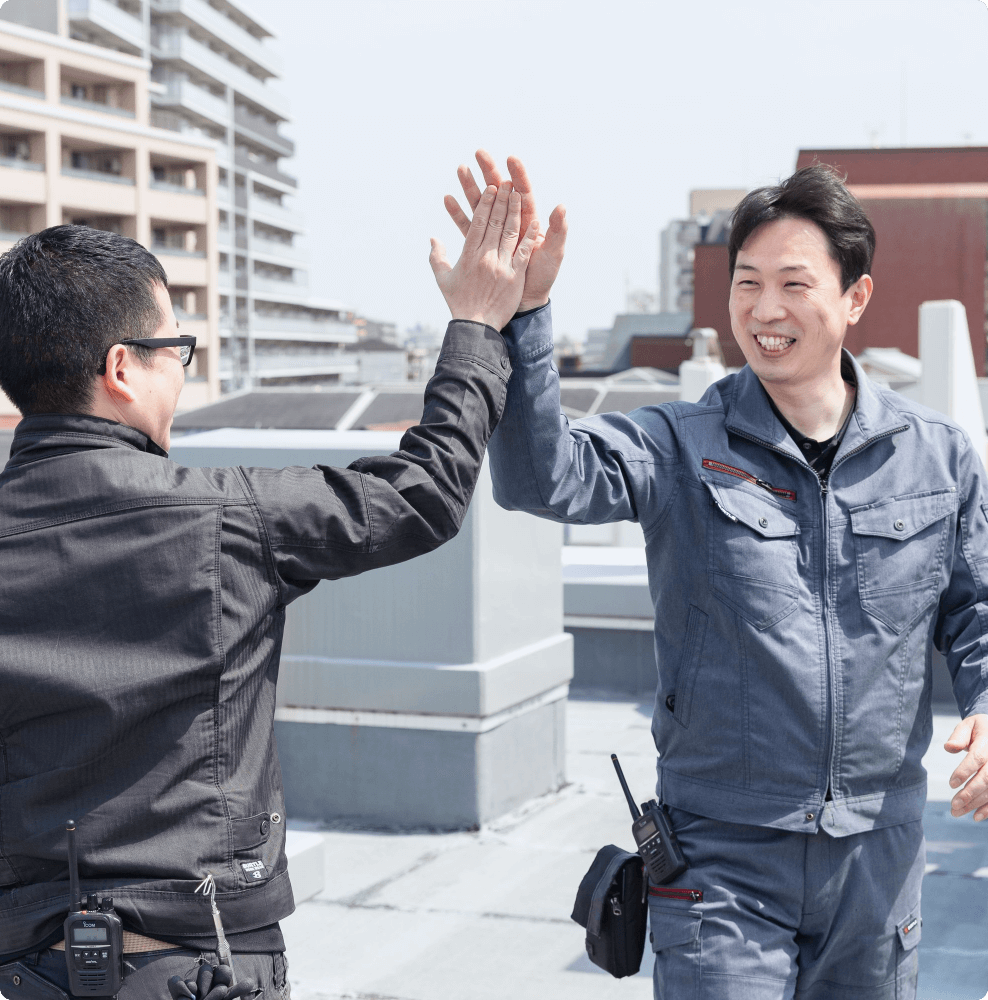 業務の達成感を分かち合い、屋上で笑顔でハイタッチを交わす2名の技術スタッフ。チームワークの強さと活気ある現場の雰囲気。